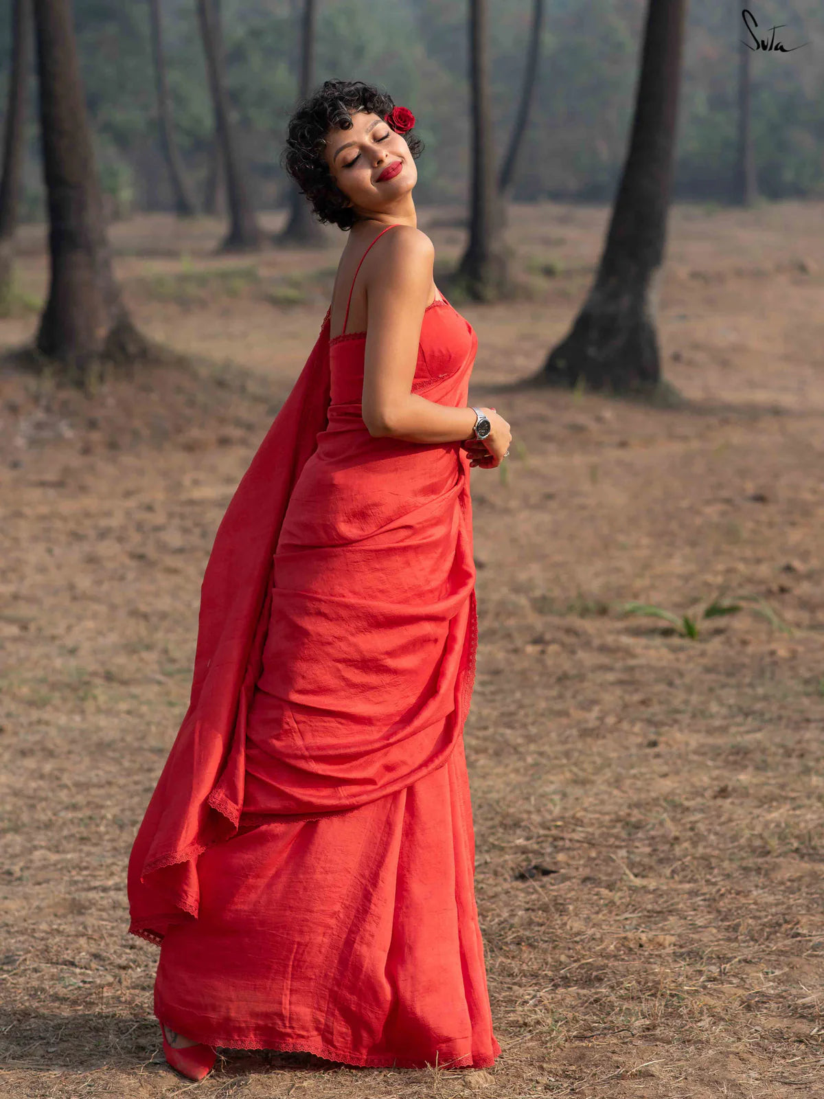Woman in a red silk saree standing in a forested area