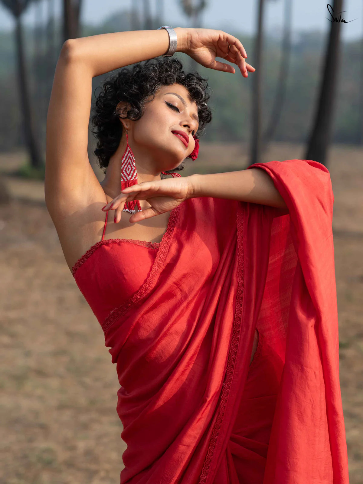 Woman in a red saree performing a dance pose outdoors.