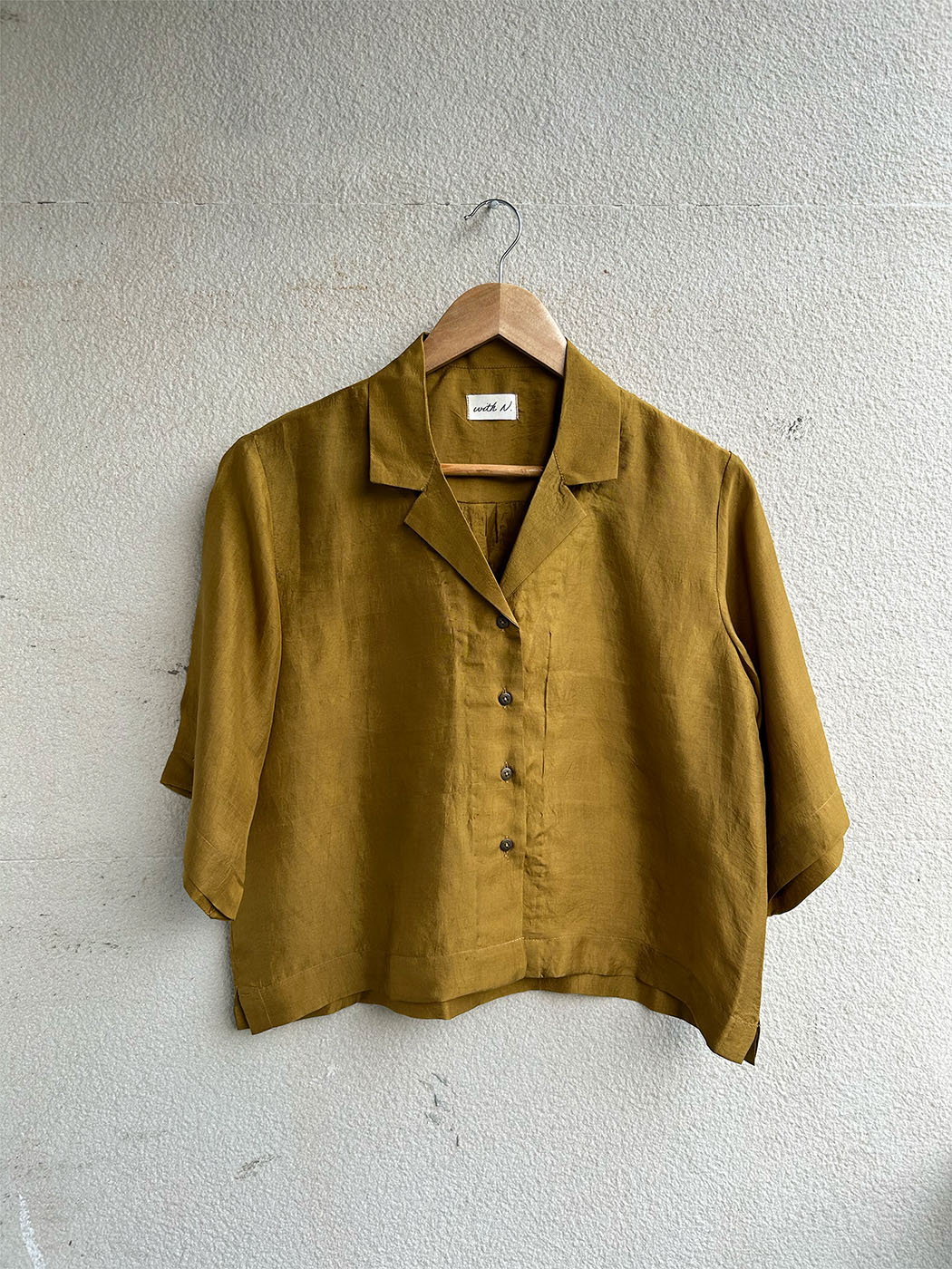 Yellow shirt on a hanger against a light gray wall