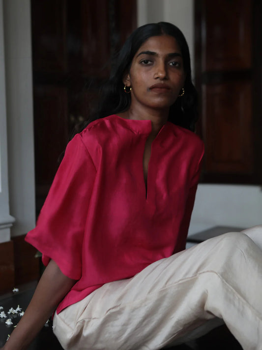 Woman wearing a bright pink top and beige pants sitting indoors.