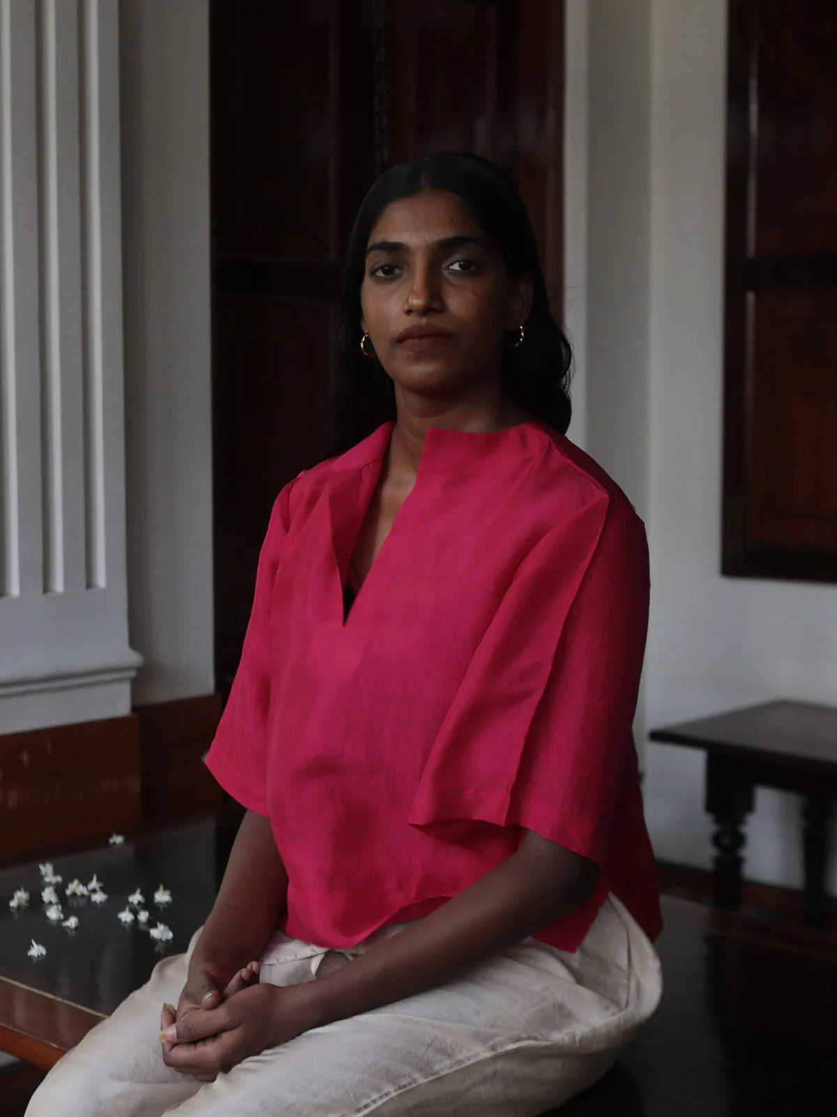 Woman wearing a bright pink blouse sitting indoors.