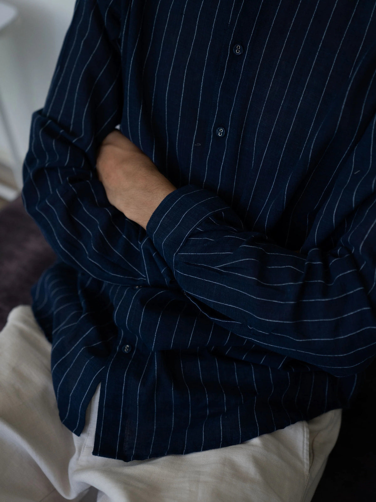 Person wearing a dark blue pinstripe shirt with a white garment underneath.
