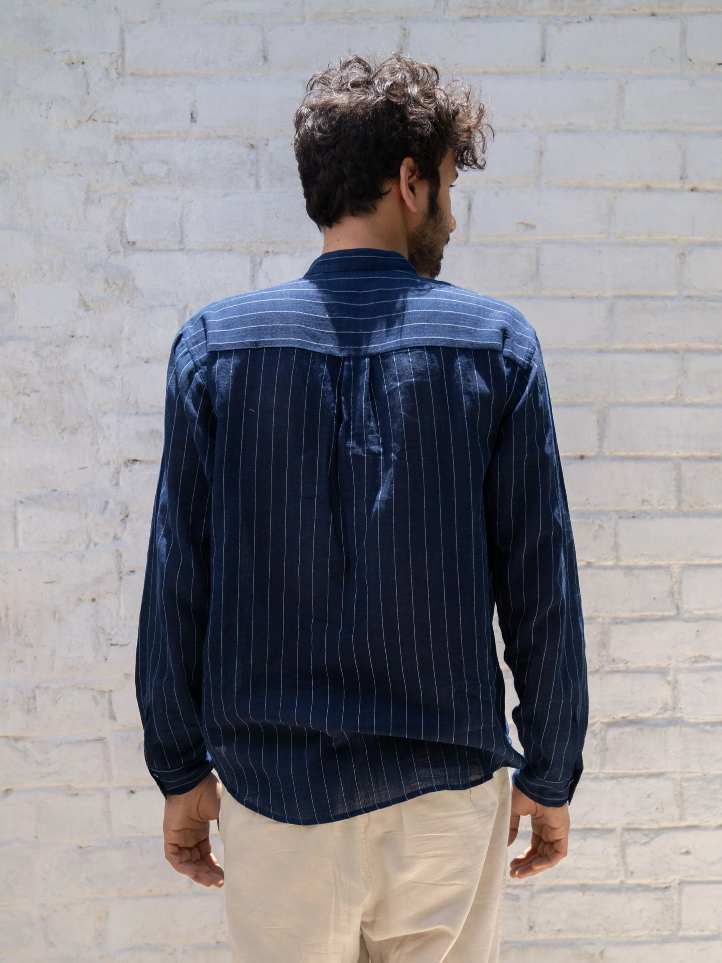 Man wearing a blue pinstripe shirt against a light brick wall