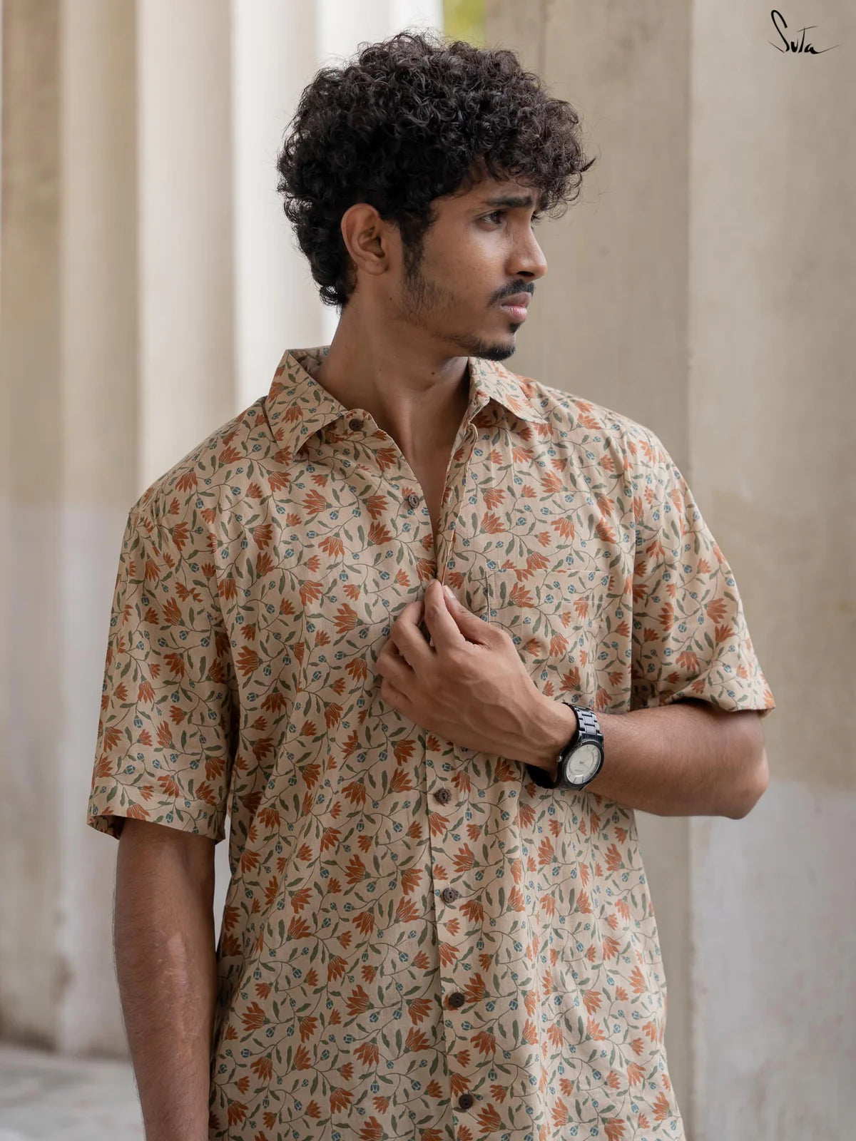 Man wearing a beige floral patterned shirt standing outdoors with columns in the background