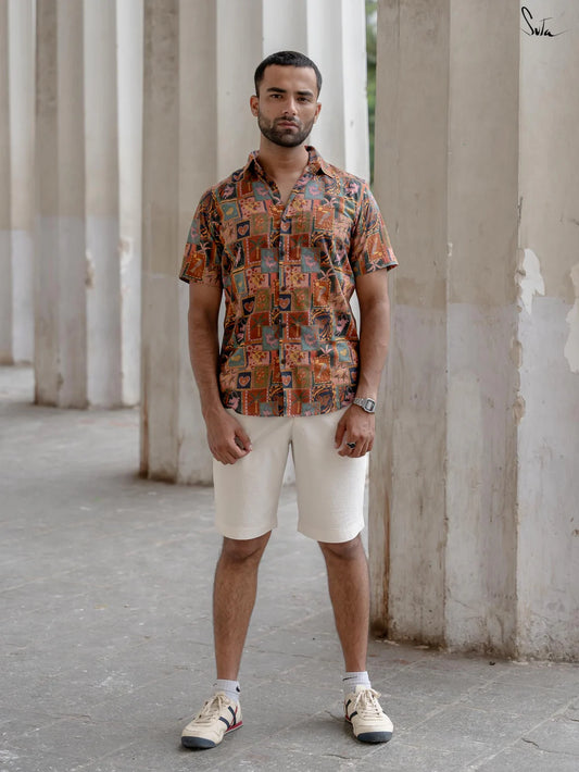 Man wearing a multicolored patterned shirt and beige shorts standing in an outdoor setting with columns.