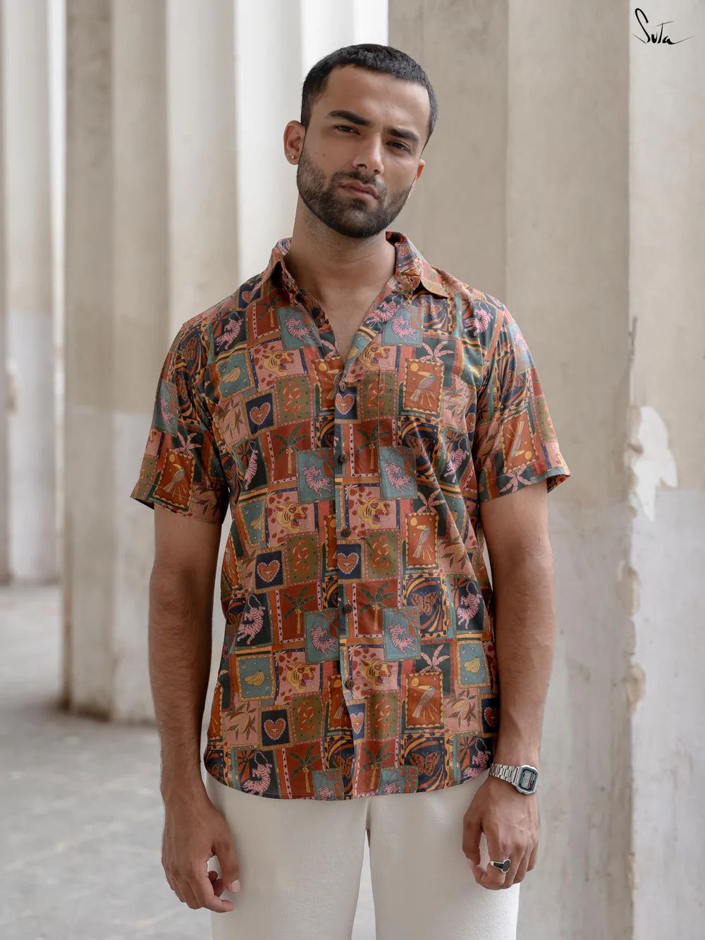 Man wearing a patterned shirt standing in front of stone columns.