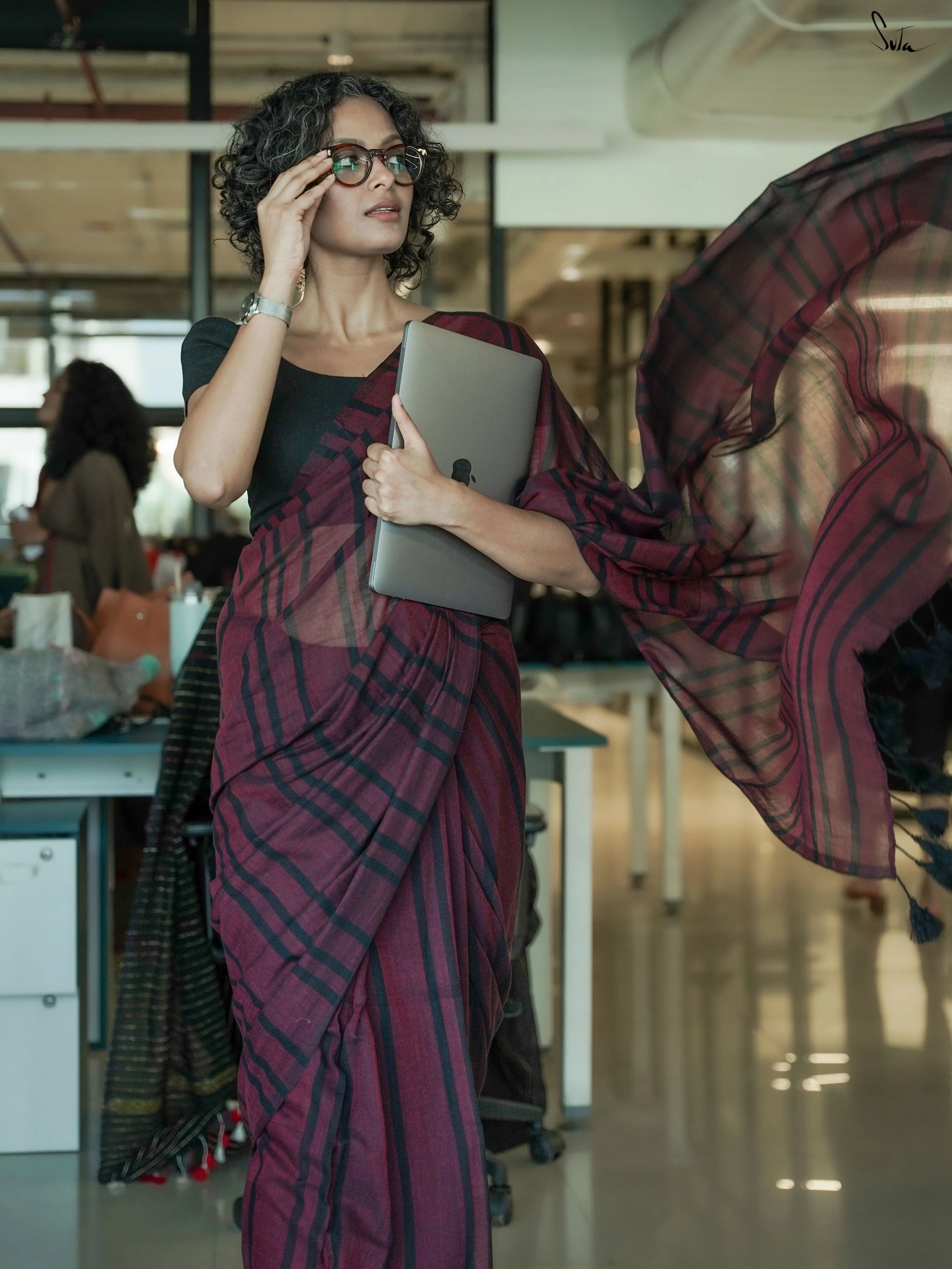Woman in a maroon saree holding a tablet in an office setting