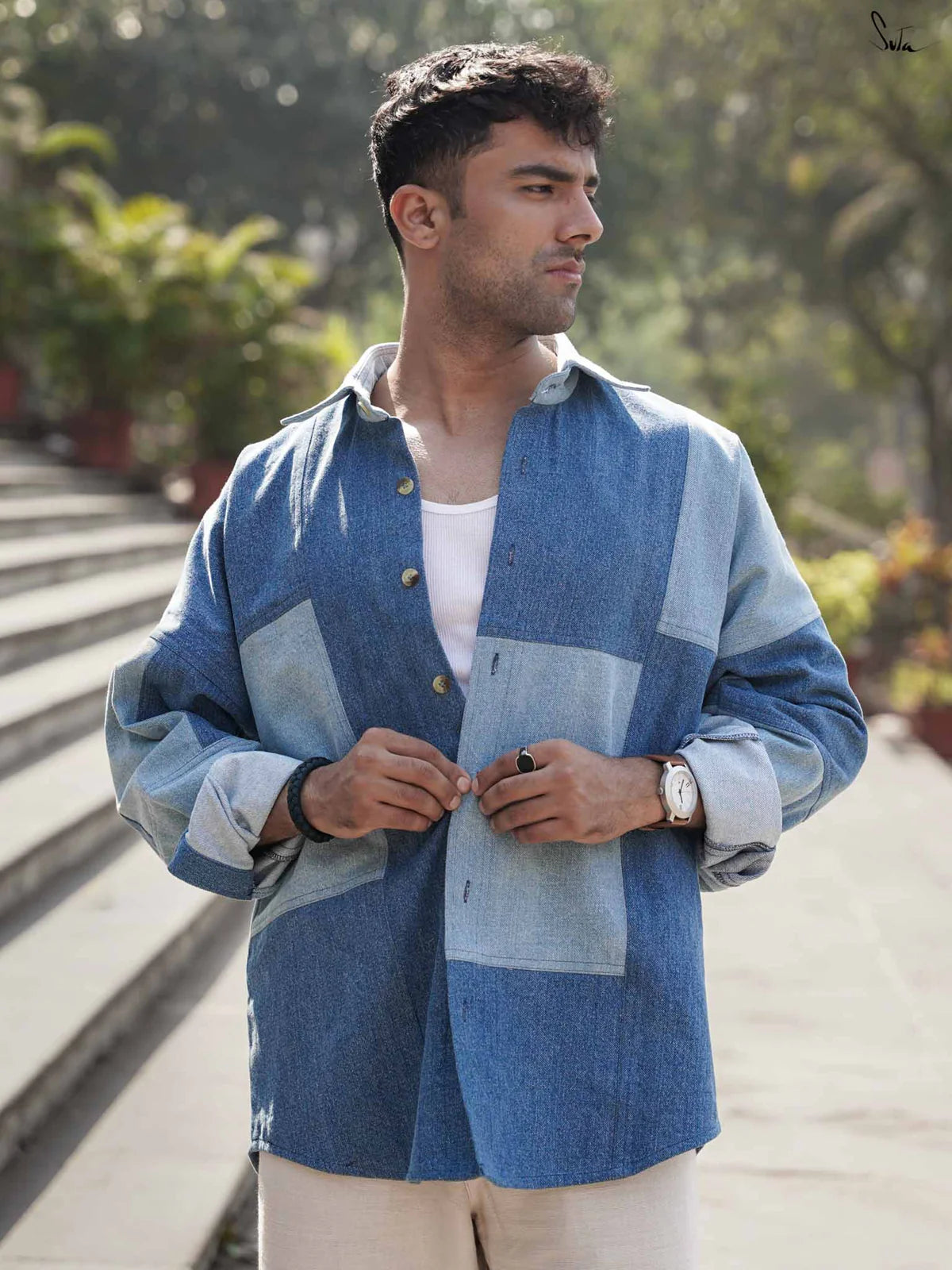 Man wearing a blue patchwork denim shirt standing on steps outdoors