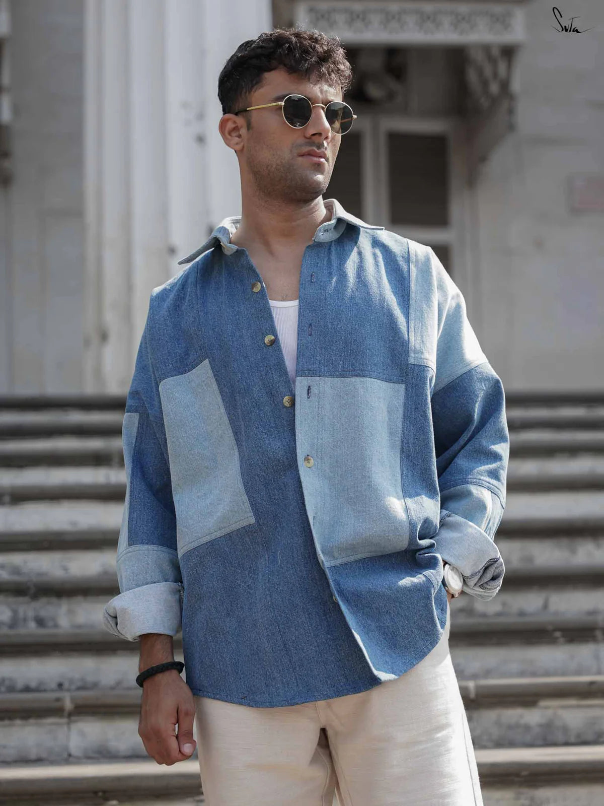 Man wearing a blue patchwork denim shirt standing on steps outdoors