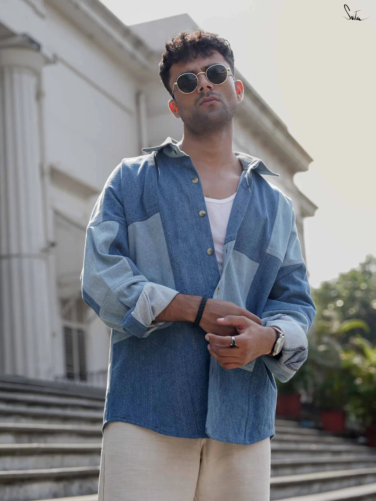 Man wearing a blue patchwork denim shirt standing on steps outdoors