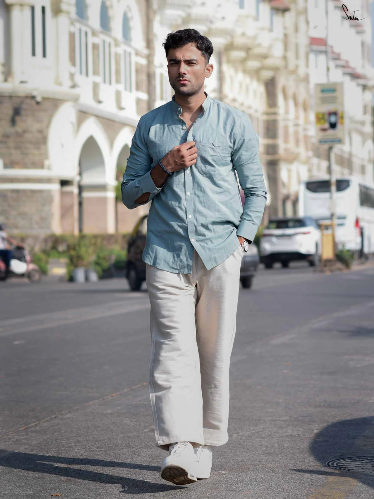 Man walking on a street wearing a light blue shirt and beige pants.