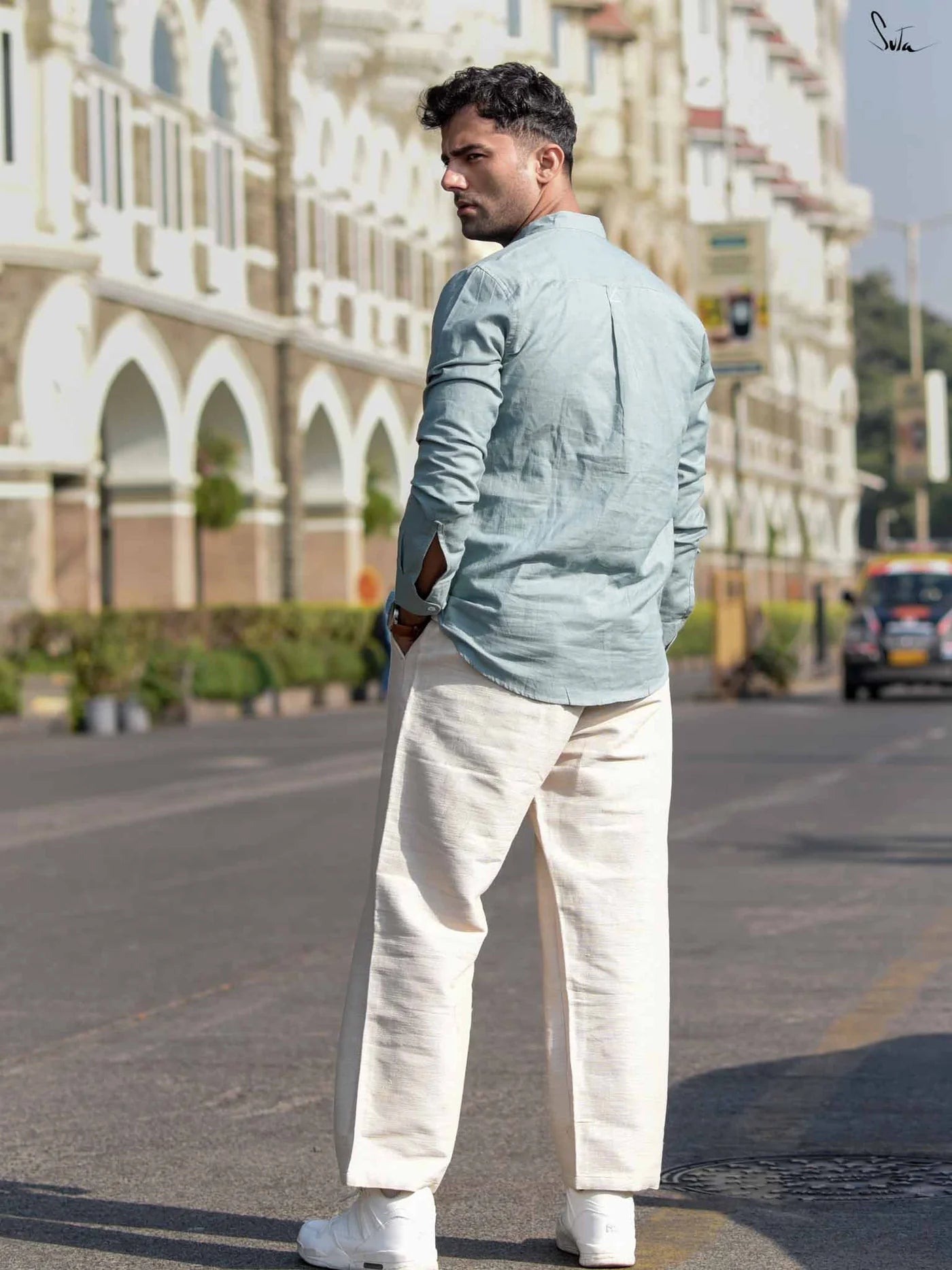 Man in light blue shirt and white pants standing on a street with buildings in the background