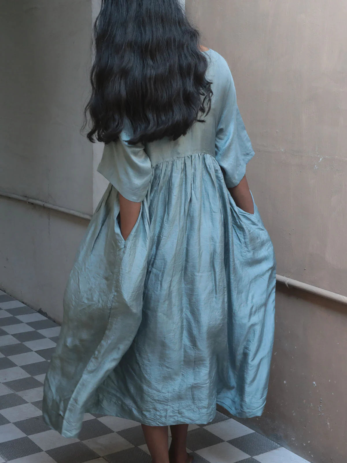 Person wearing a light blue dress with pockets n the sides in an indoor setting.