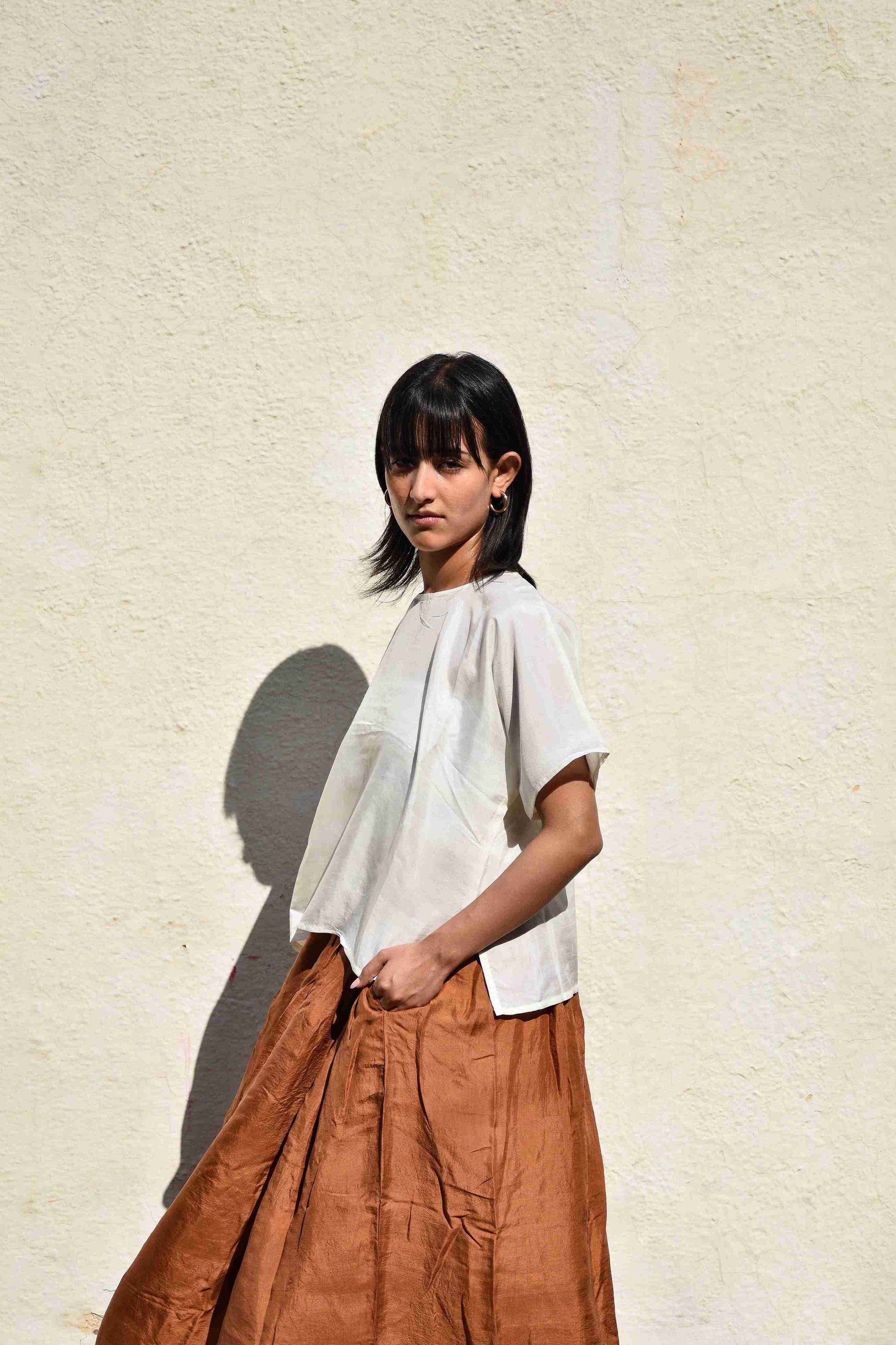 Woman wearing a white top and brown skirt against a light beige wall