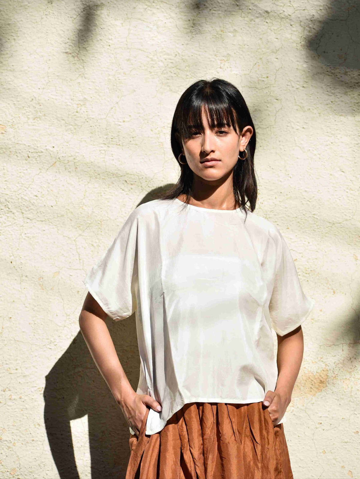 Woman wearing a white top and brown skirt against a textured wall.