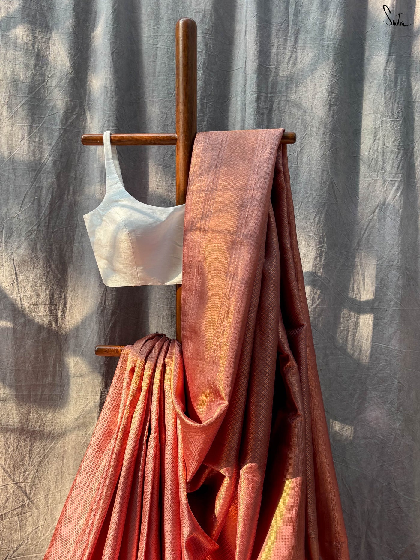 Red and Gold saree fabric draped over a wooden stand against a textured wall.