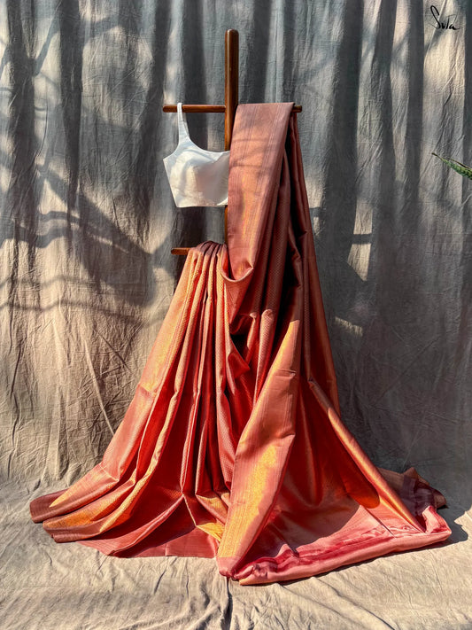 Red and Gold saree fabric draped over a wooden stand against a textured wall.