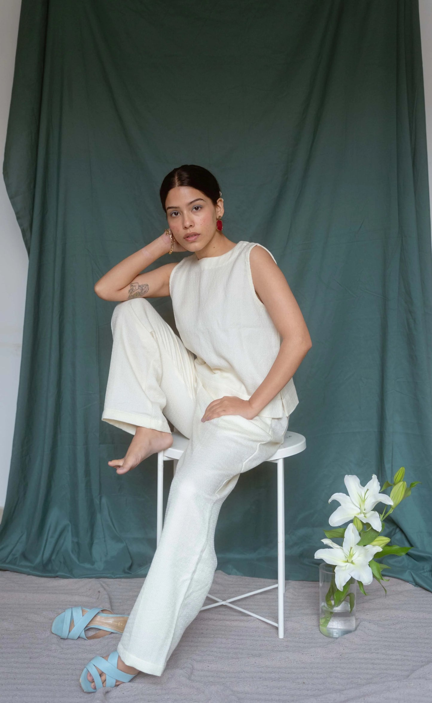 Woman in a white outfit sitting on a chair with a green curtain background