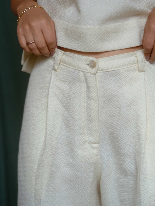 Person wearing a white top and light-colored pants with a blurred background