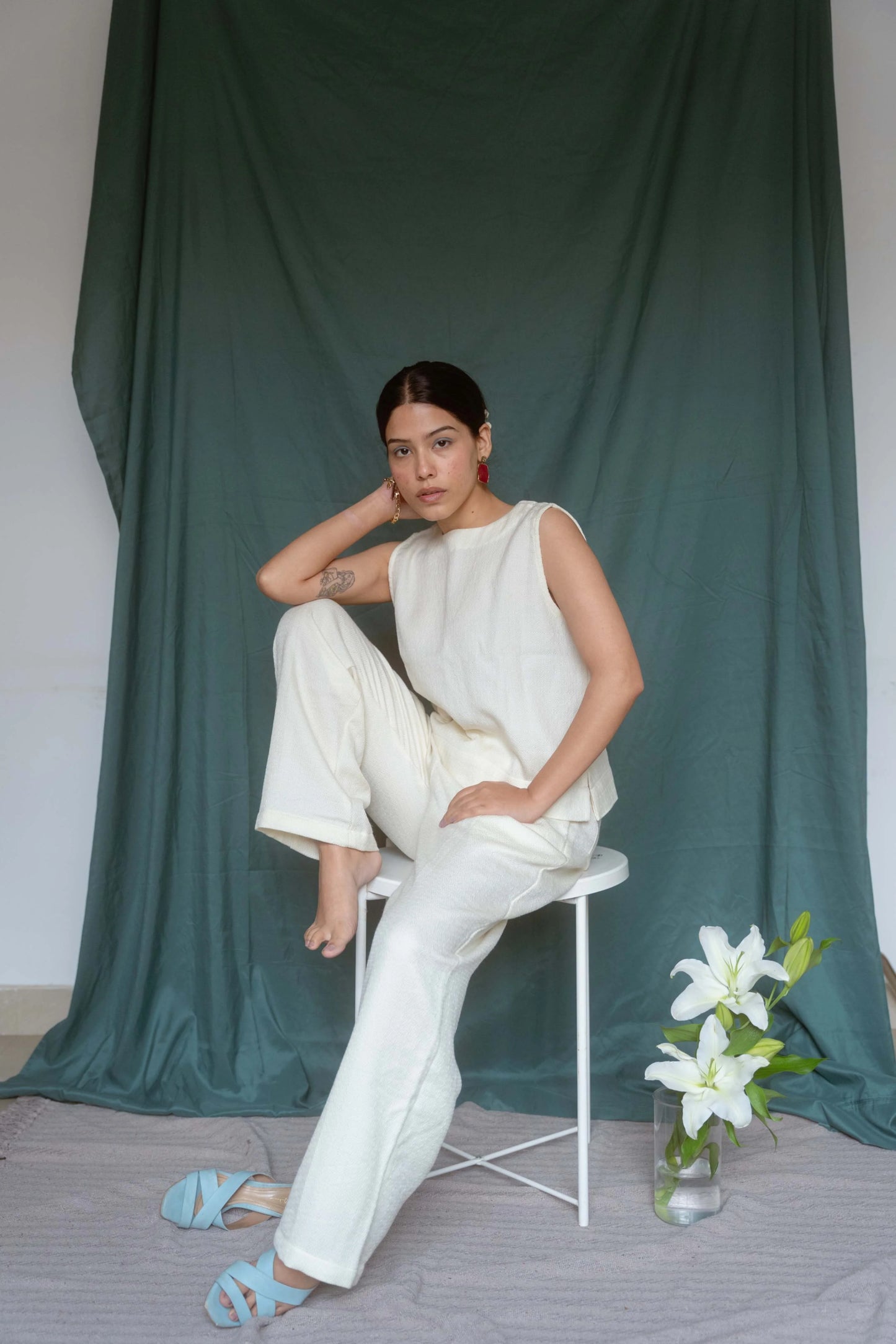 Woman in a white outfit sitting on a chair against a green curtain