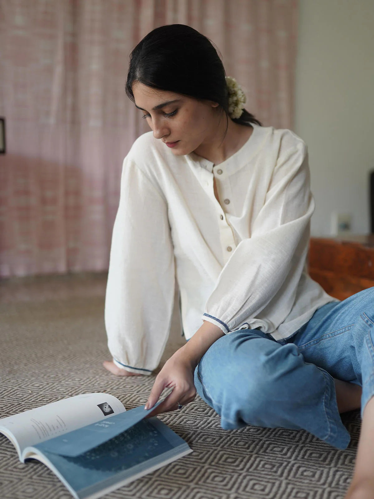 Woman reading a book on the floor wearing a beige shirt with a blurred background