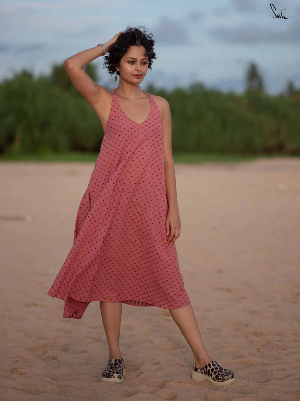 Woman in a pink dress standing on a beach with greenery in the background