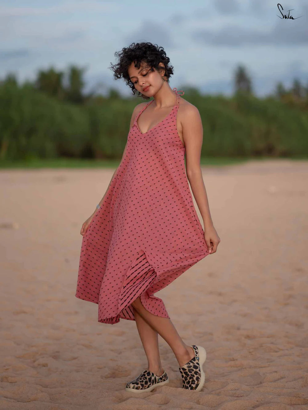 Woman in a pink dress standing on a beach with greenery in the background