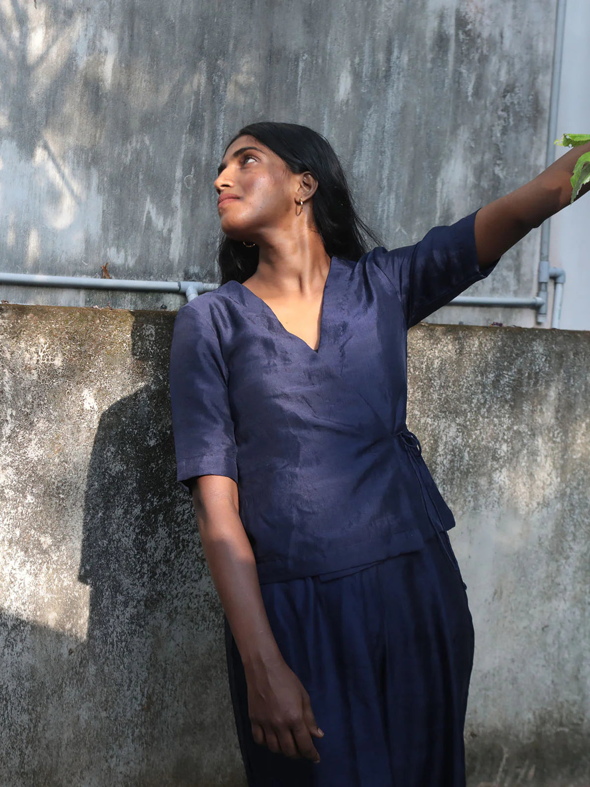 Woman in a navy blue outfit standing against a textured wall.