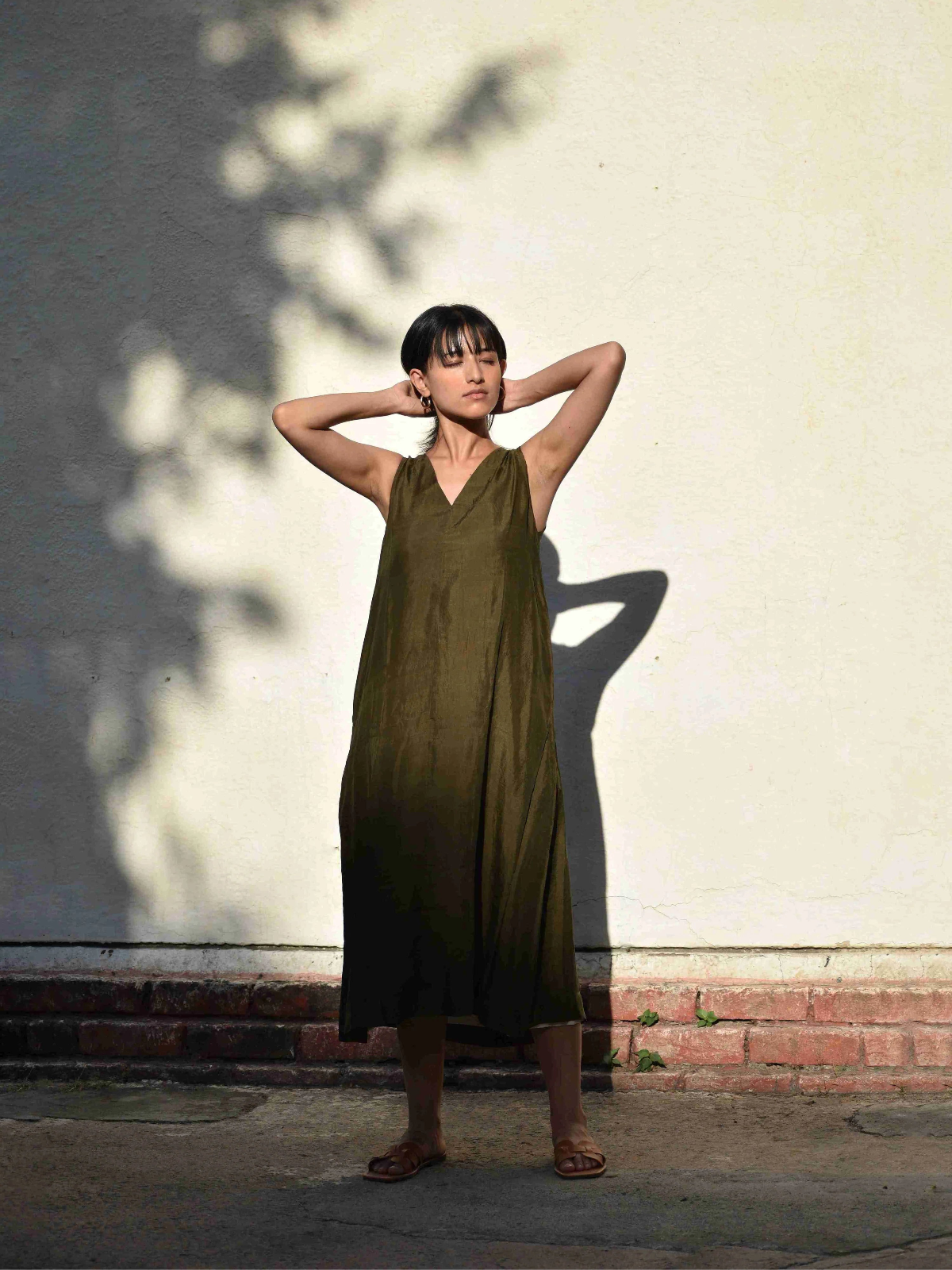 Woman in a green dress standing against a light-colored wall with shadows.