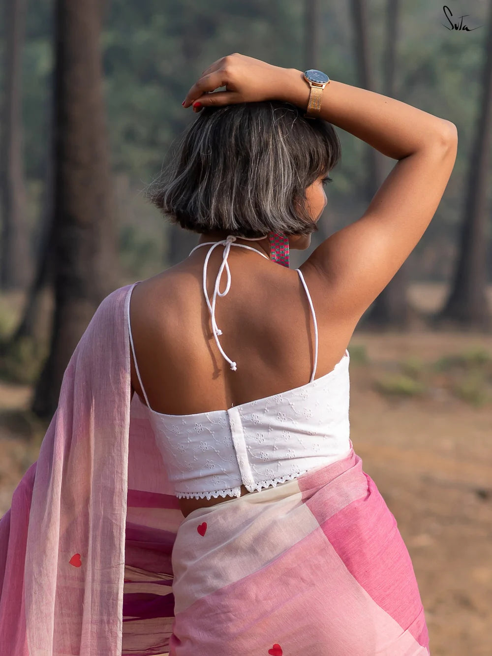 Woman in a white blouse and pink saree standing outdoors with trees in the background