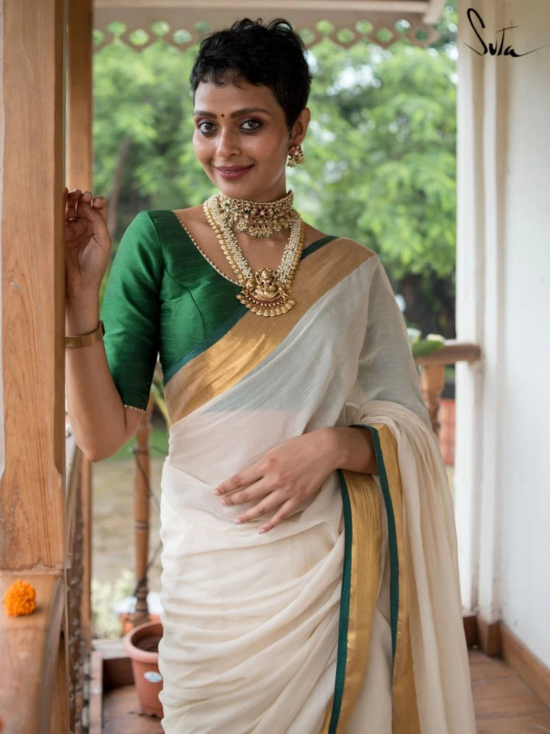 Woman in a green and white saree with gold border indoors