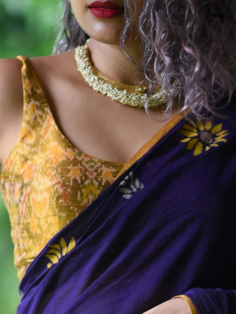 Person wearing a yellow blouse with ikat patterns and a purple saree, accessorized with a gold necklace.