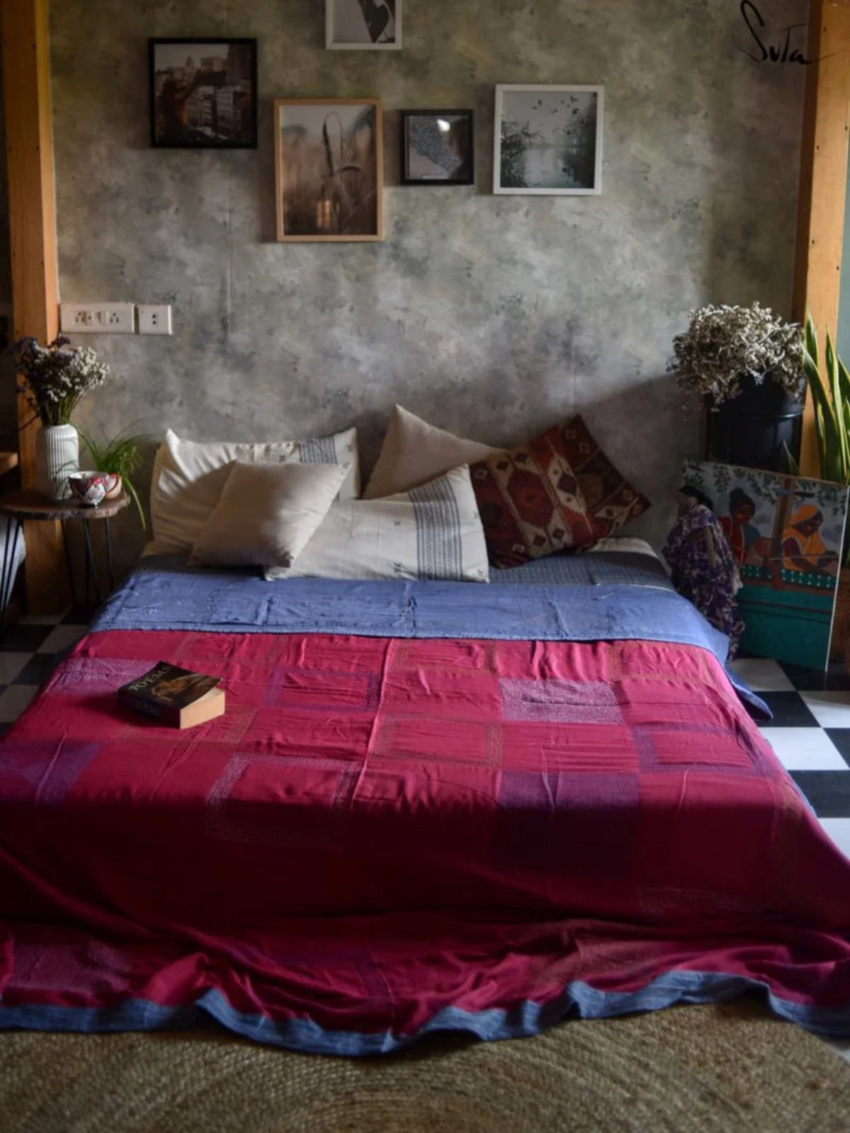Bedroom with a bed covered in a red and blue quilt, surrounded by framed pictures on the wall.