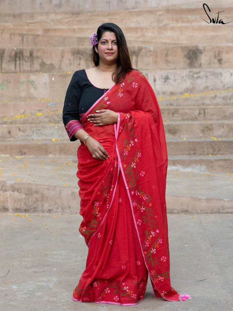 Woman wearing a red saree with floral patterns in front of stone steps.