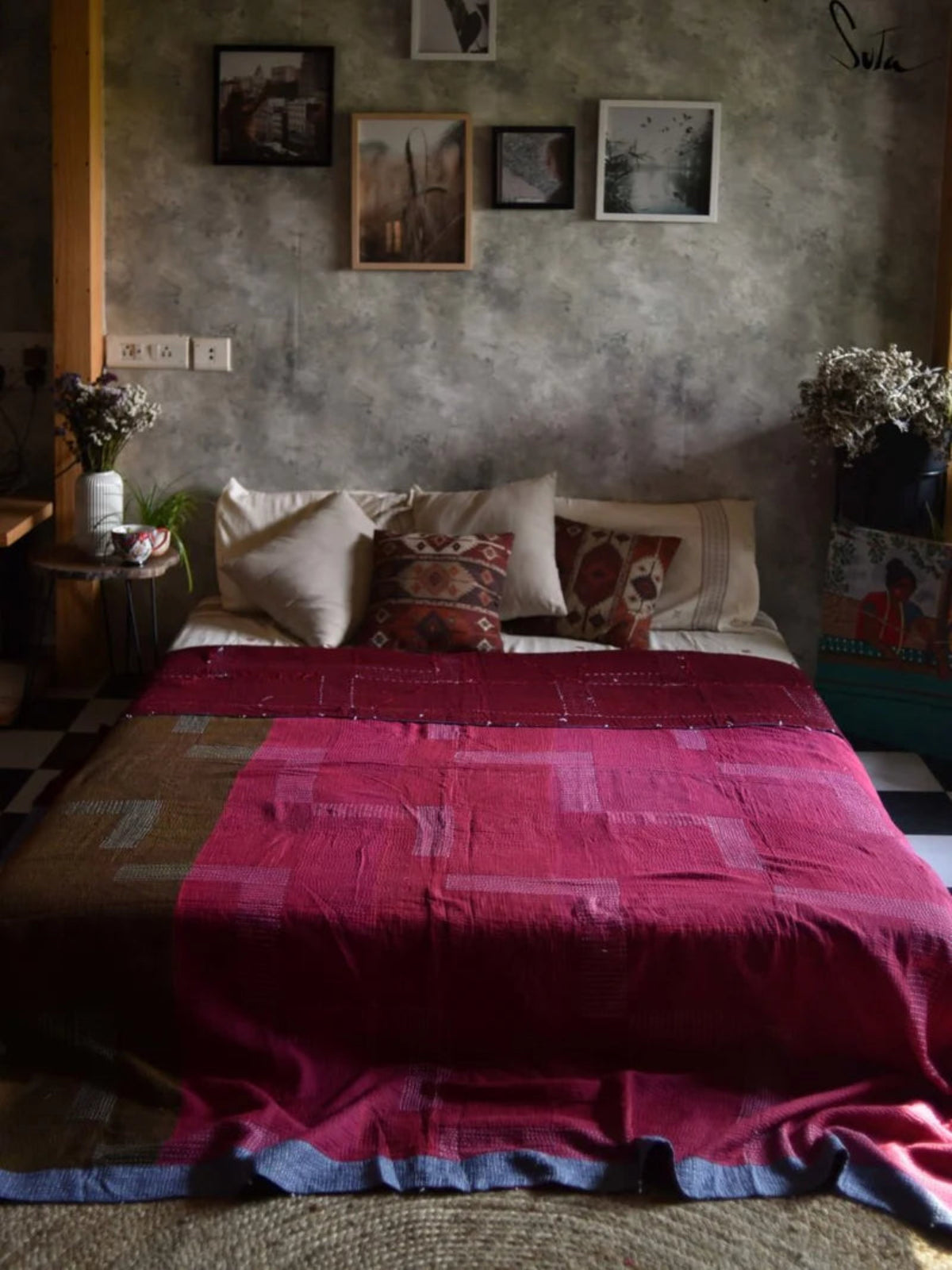 Bedroom with a bed covered in a red quilt, pillows, and framed pictures on the wall.