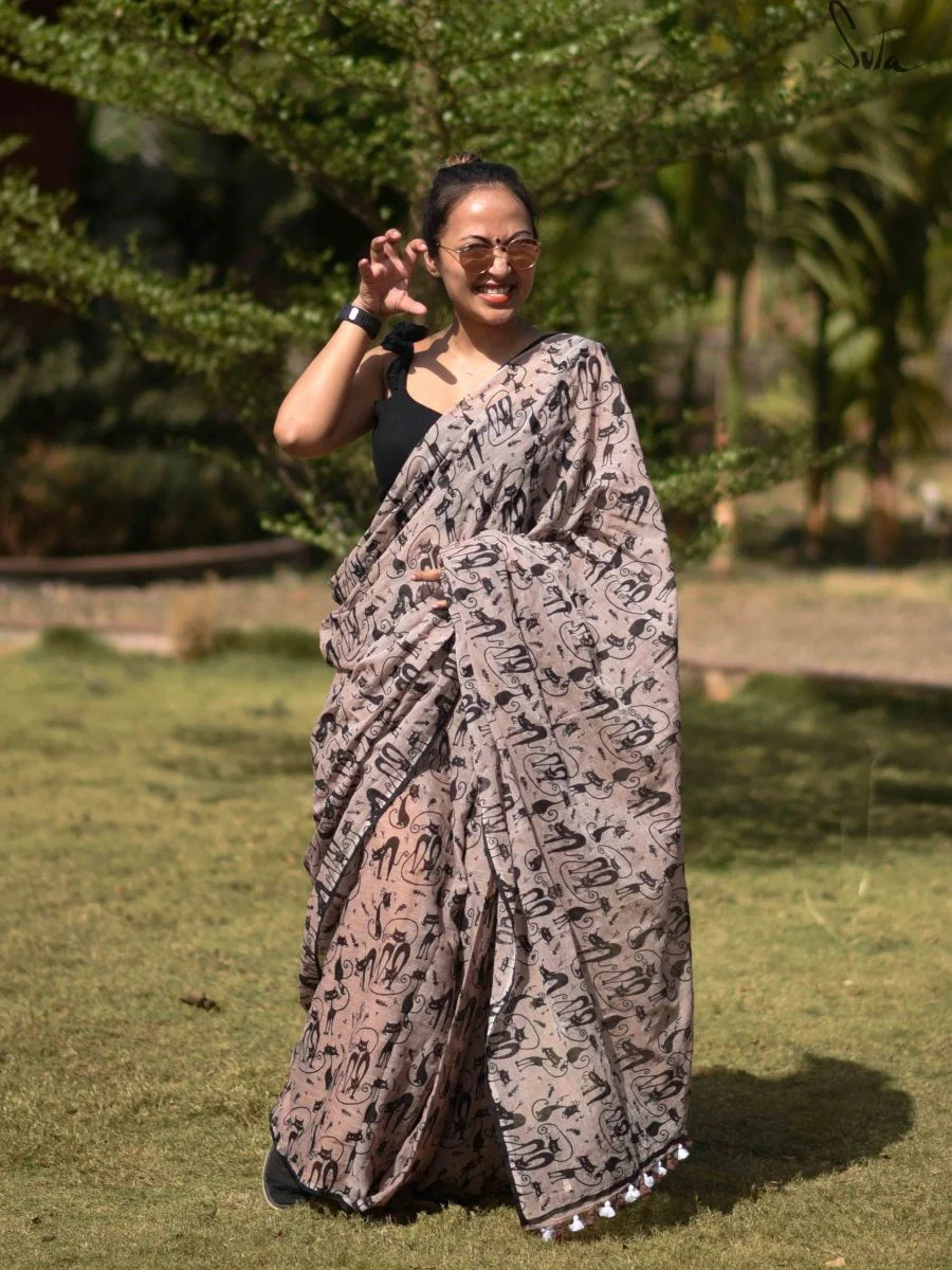 Woman wearing a patterned saree outdoors with greenery in the background