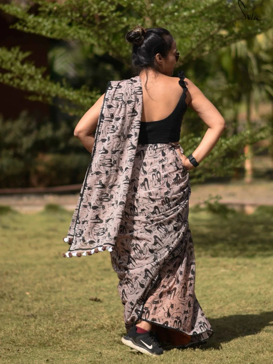 Woman wearing a patterned saree standing outdoors with greenery in the background