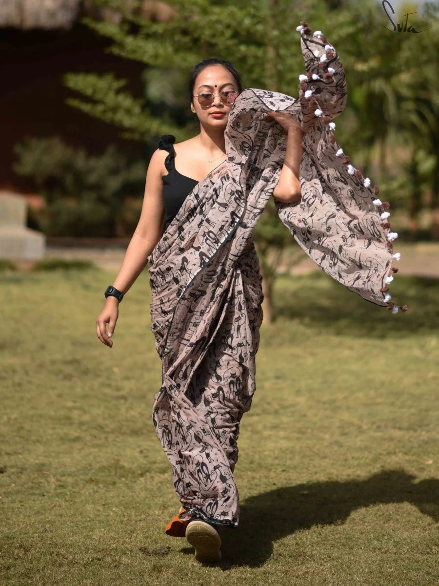 Woman in a saree with a pattern walking outdoors on grass.