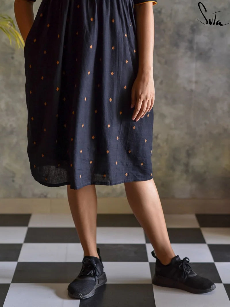 Person wearing a black dress with gold polka dots on a checkered floor.