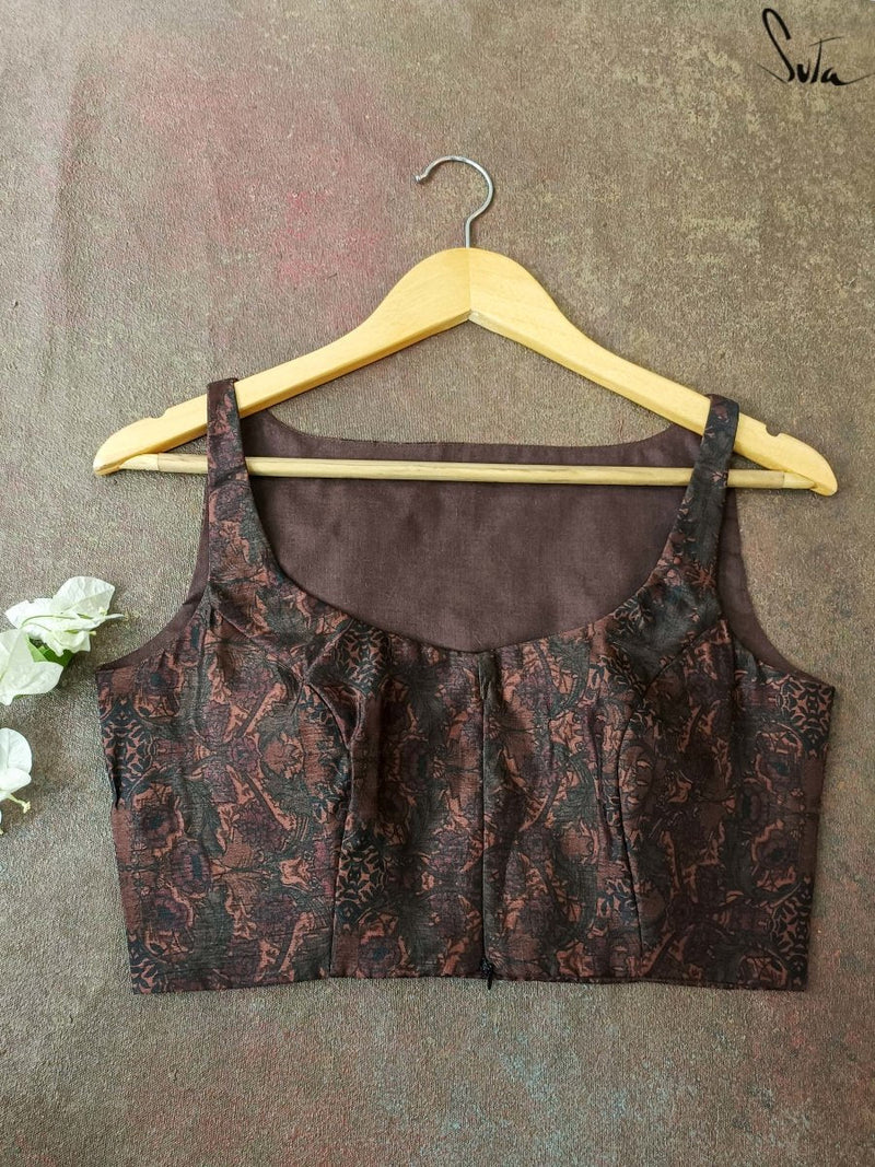 Brown patterned blouse on a hanger against a textured gray background