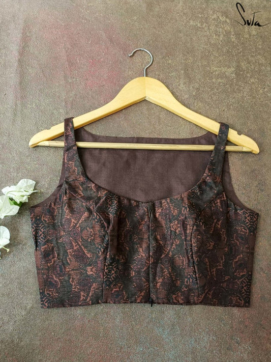 Brown patterned blouse on a hanger against a textured gray background