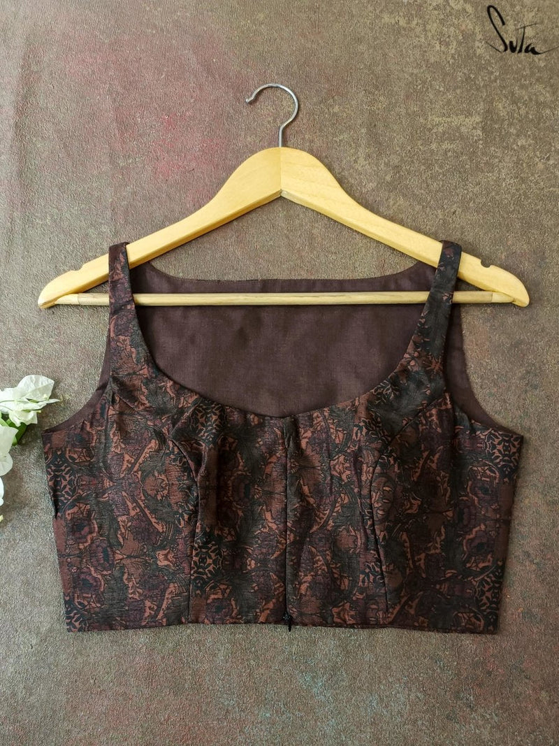 Brown patterned blouse on a hanger against a textured gray background