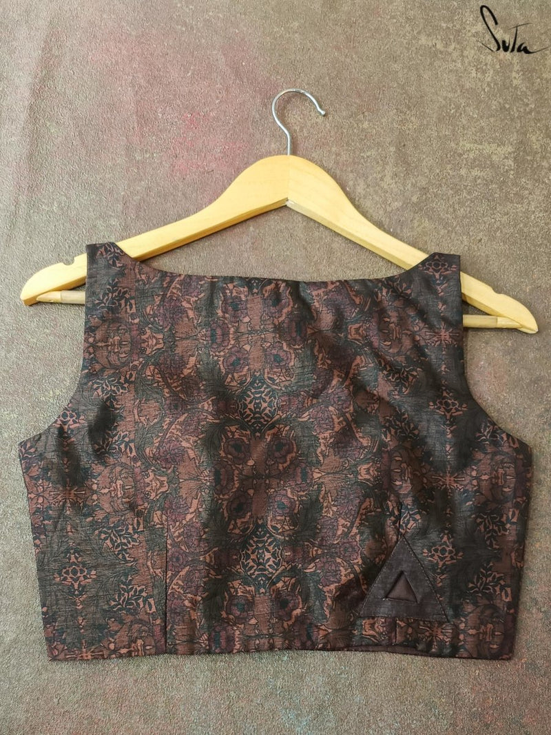 Brown patterned blouse on a hanger against a textured gray background