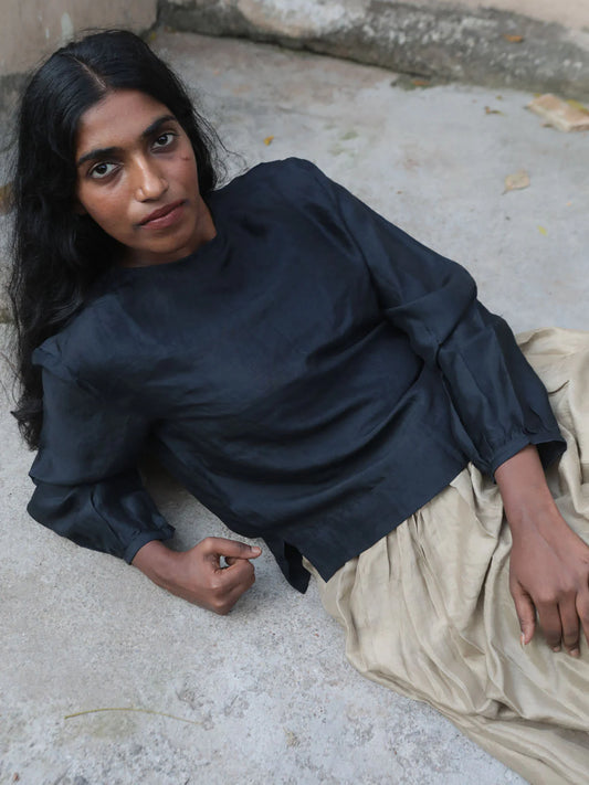 Woman sitting on a stone surface wearing a black top and beige skirt.
