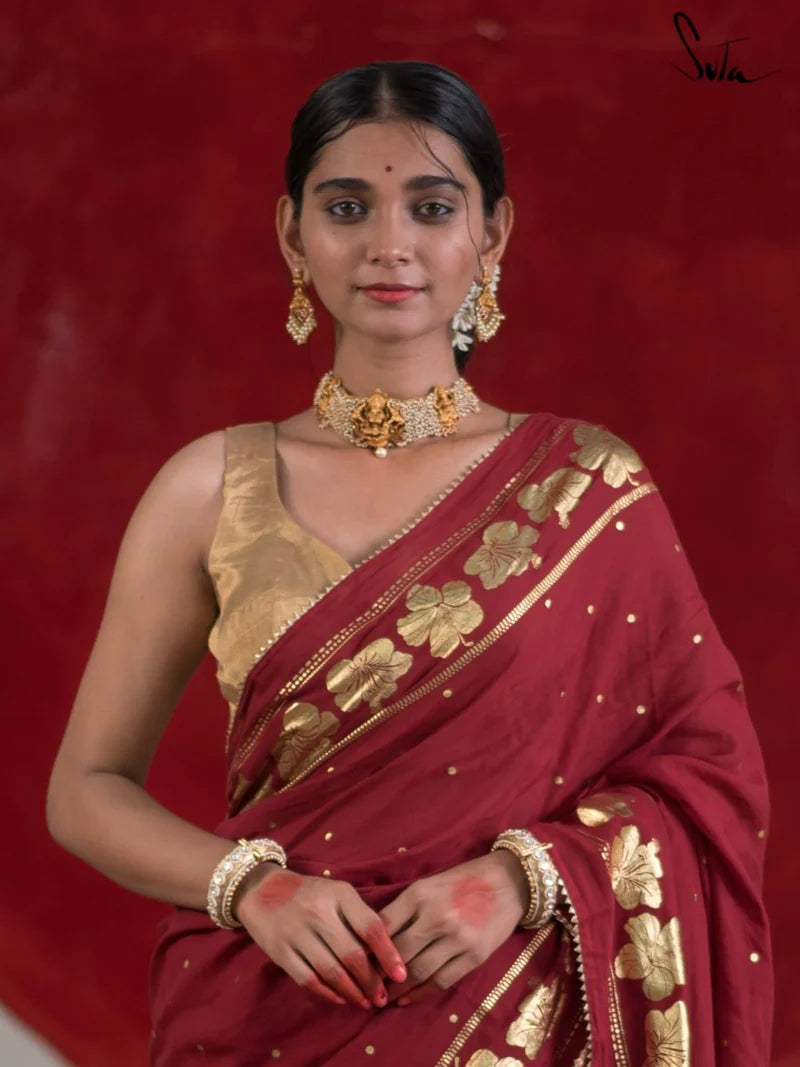 Woman in a red saree with gold details , with a gold blouse against a red background