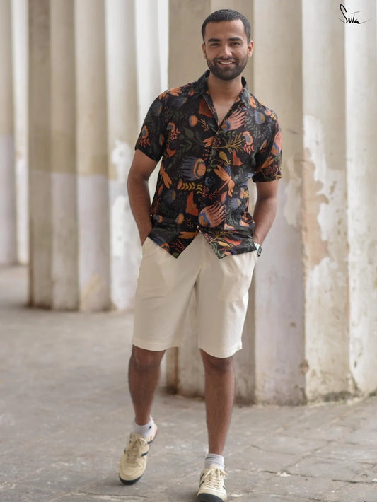 Man wearing a patterned shirt and beige shorts standing in front of columns.
