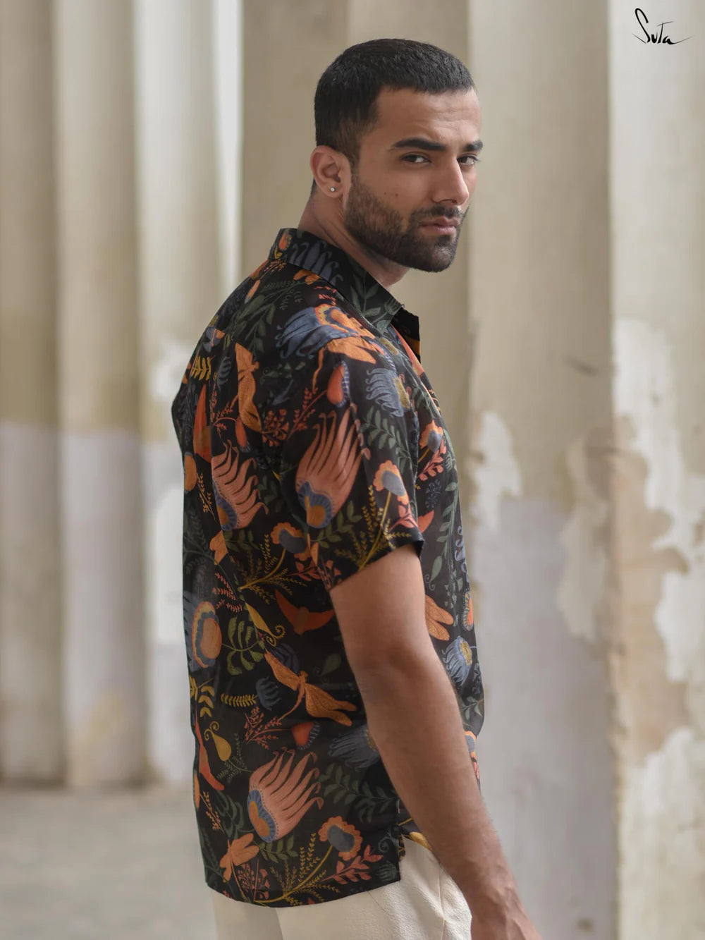 Man wearing a patterned shirt standing in a room with columns.