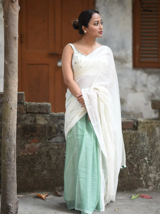 Woman wearing a white and green saree standing outdoors.