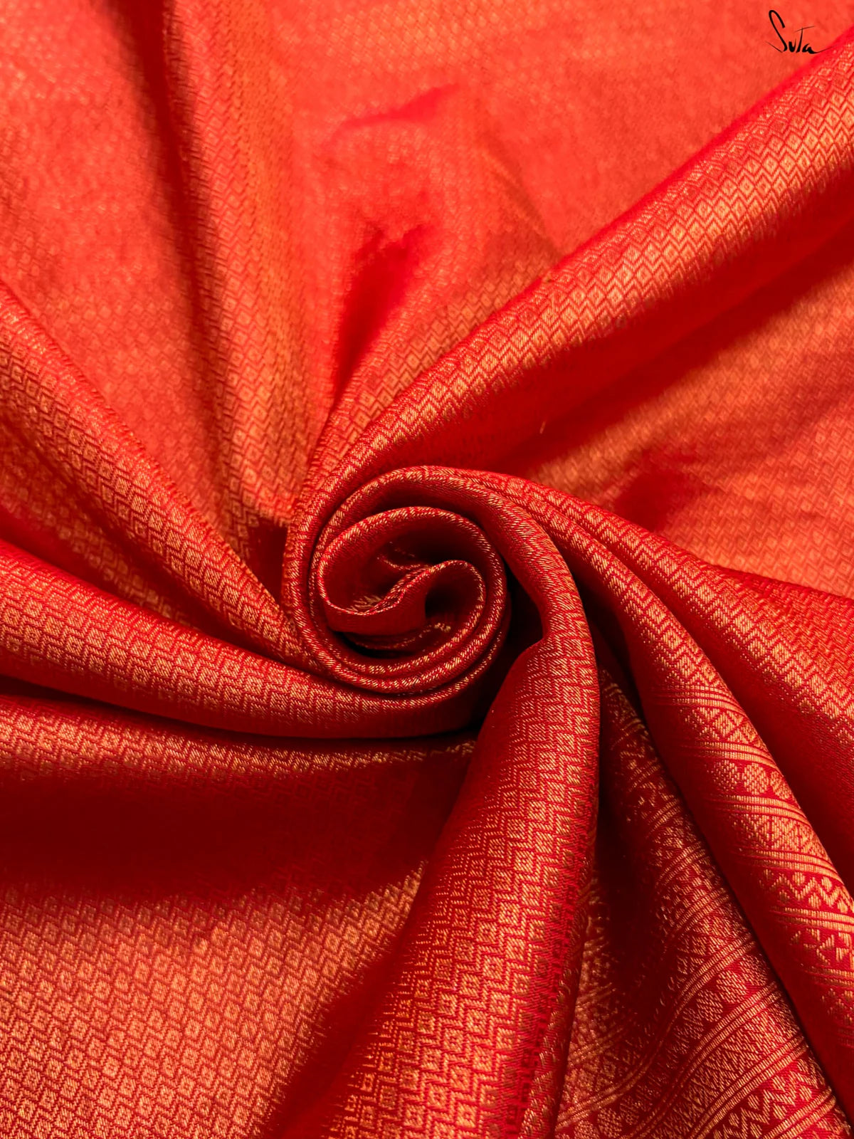Close-up of red fabric with a subtle pattern made with gold zari