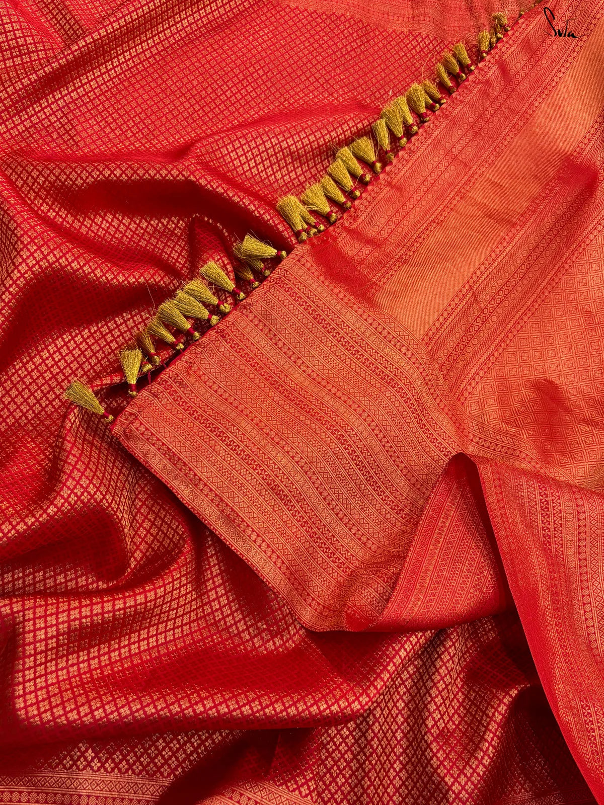 Close-up of a red silk saree fabric with a gold tassel detail